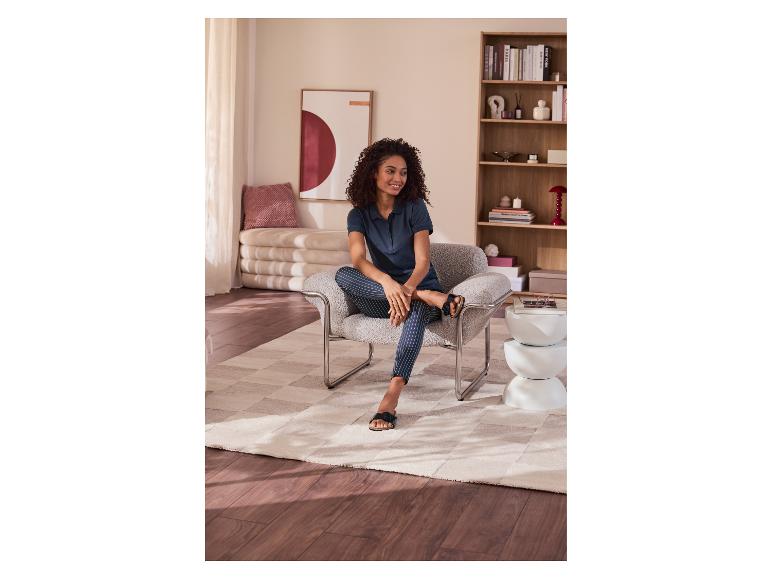 Frau sitzt in einem Sessel mit gestreiften Hosen und Poloshirt, in einem gemütlichen Wohnzimmer.