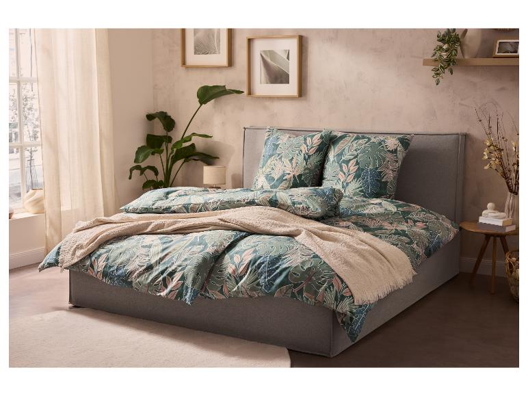 Bett mit tropischer Bettwäsche, Pflanzen und Bildern in einem Schlafzimmer.
