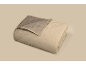 Gefaltete beige Steppdecke mit einer graubraunen Innenseite und rautenförmigen Nähten.
