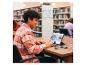 Lächelnde junge Person benutzt ein Tablet mit Tastatur in einer Bibliothek.