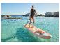 Frau in Schwimmweste beim Stand-Up-Paddling in klarem Wasser mit Felsen.