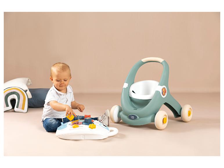 Baby spielt mit Aktivitätsbrett und einem Little Smoby Lauflernwagen im Hintergrund.
