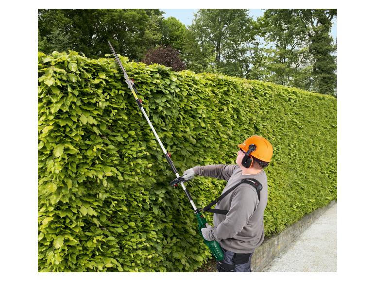 Mann schneidet Hecke mit einer Parkside Teleskop-Heckenschere, mit Helm und Gehörschutz.