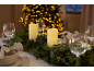 Weihnachtstisch dekoriert mit Kerzen, Stechpalmen- und Tannengirlande, und beleuchtetem Weihnachtsbaum im Hintergrund.