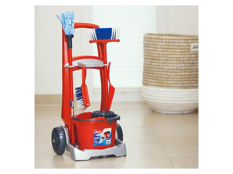 Roter Vileda Junior Putzwagen mit Zubehör, neben einem geflochtenen Korb.