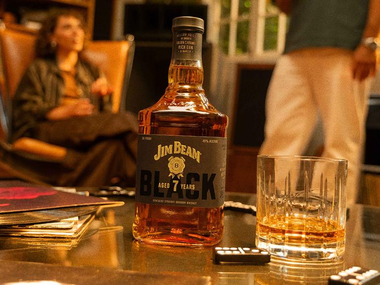 Jim Beam Black Bourbonflasche und Glas auf einem Tisch mit Personen im Hintergrund.