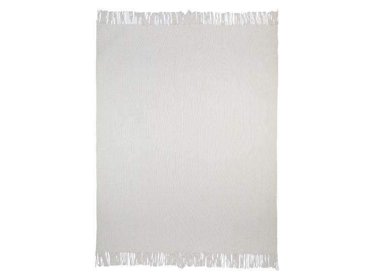 Eine cremefarbene gestrickte Decke mit Fransen.