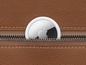 Ein weißer Apple AirTag in einer Ledertasche.