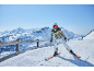 Frau fährt Ski in den Bergen, trägt grüne Jacke, weiße Hose, Helm und Brille.