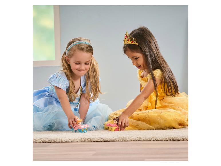 Zwei Mädchen in Prinzessinnenkleidern spielen mit Spielzeugprinzessinnen auf einem Teppich.