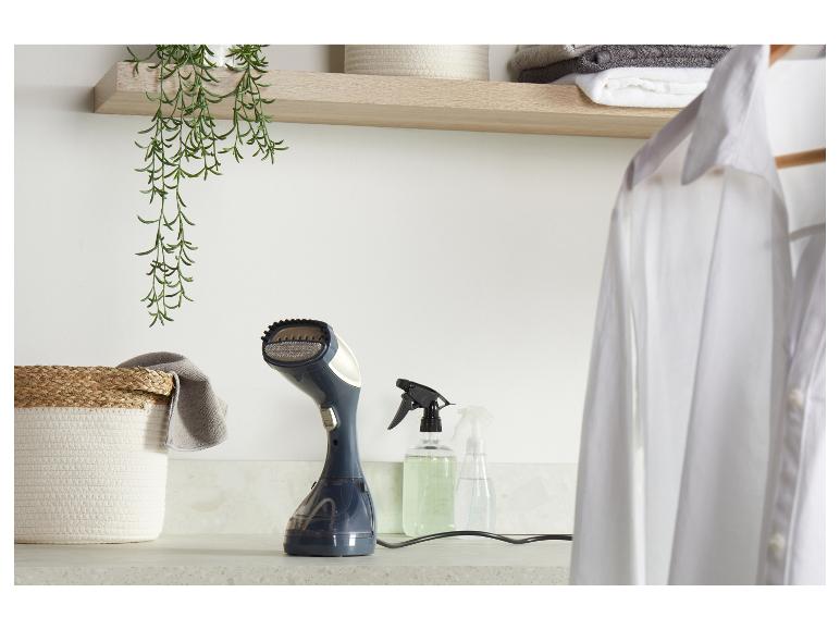 Ein Handdampfglätter auf einer Arbeitsplatte mit einem weißen Hemd, Korb und Sprühflaschen.