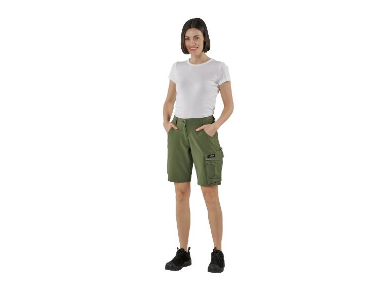 Lächelnde Frau in weißem T-Shirt und olivgrünen Cargo-Shorts mit schwarzen Stiefeln.