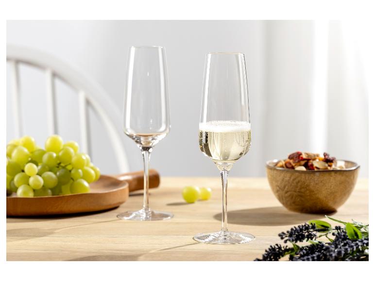 Zwei Sektgläser, eines gefüllt mit Sekt, mit Trauben und Nüssen auf einem Tisch.