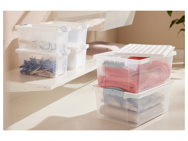 Transparente Aufbewahrungsboxen mit Deckeln, gefüllt mit Handtüchern und Wäscheklammern.