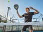 Mann spielt Padel mit Schläger, Ball und Platz im Hintergrund.
