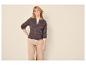 Frau in brauner Strickjacke und beiger Hose, posiert mit der Hand in der Hüfte.