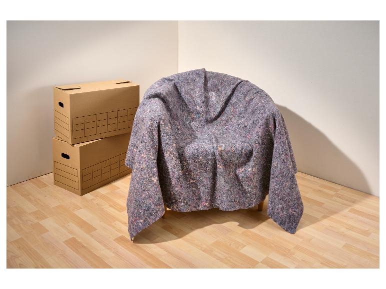 Sessel mit Umzugsdecke und Stapel Kartons in einer Zimmerecke.