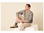 Mann sitzt in beigem Strickpullover und Hose, mit beigen Stiefeletten.