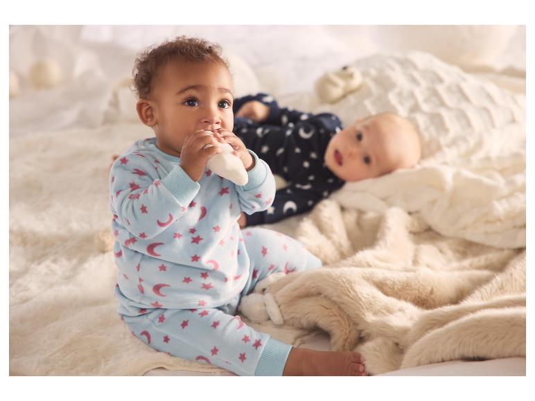 Zwei Babys in weichen Schlafanzügen, eines sitzend und das andere liegend auf einer flauschigen Decke.
