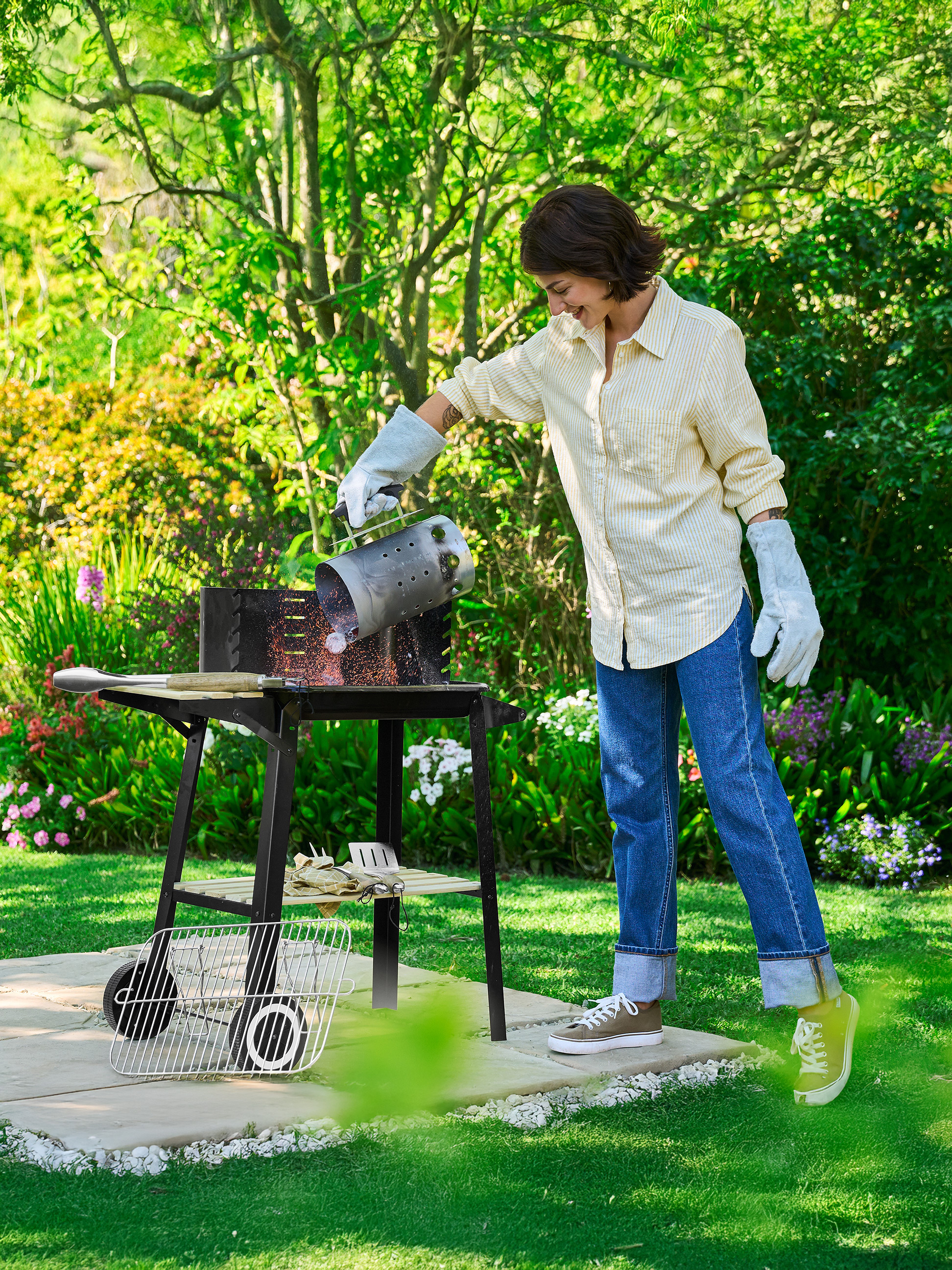 Frau schüttet Kohle aus einem Anzündkamin in einen Outdoor-Grill.