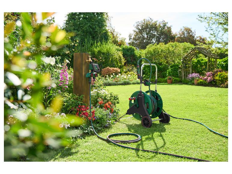 Gartenschlauch auf Rollwagen und Bewässerungstimer an Holzpfosten im Garten.