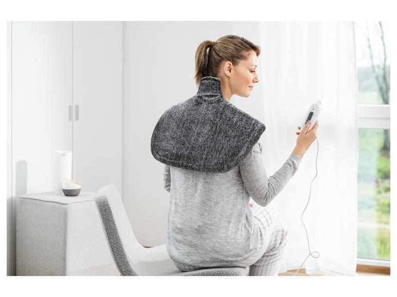 Frau trägt ein elektrisches Heizkissen auf den Schultern und hält eine Fernbedienung.