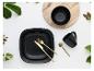 Schwarzes Geschirr mit goldenem Besteck, Schale und Tasse auf Holz und weißem Hintergrund mit Blättern.