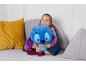 Lächelndes Mädchen umarmt blaues Plüschtier auf grauem Sofa mit Kissen.