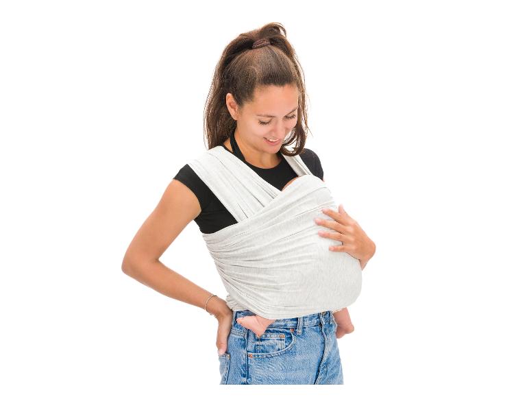 Frau mit braunen Haaren in schwarzem T-Shirt und Jeans, die ein Baby in einer grauen Trage trägt.