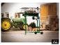 Grüner Holzspalter mit Holzscheit, auf einem Bauernhof mit Traktor im Hintergrund.