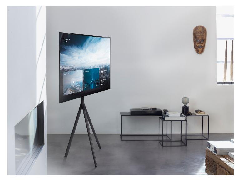 Ein moderner Fernseher auf einem Stativ, der eine Smart-Home-Oberfläche mit Uhrzeit, Wetter und Medienoptionen anzeigt.