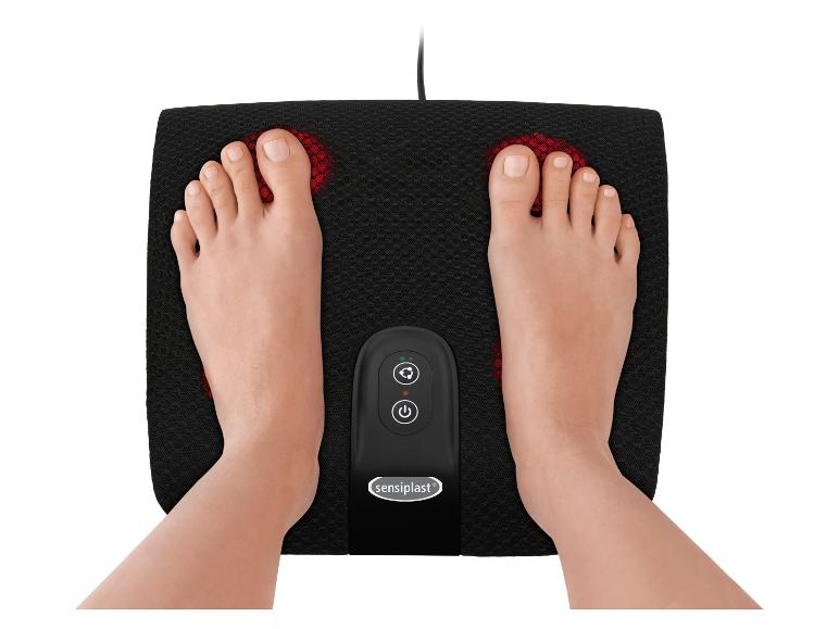 Füße auf einem schwarzen elektrischen Fußmassagegerät mit roten Lichtern und Bedienfeld.