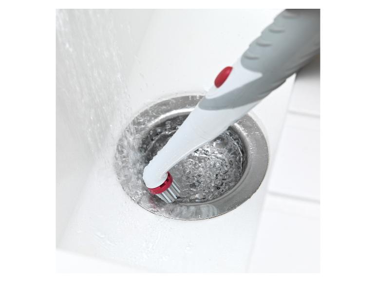 Eine Bürste mit rotem Knopf reinigt ein Waschbecken.