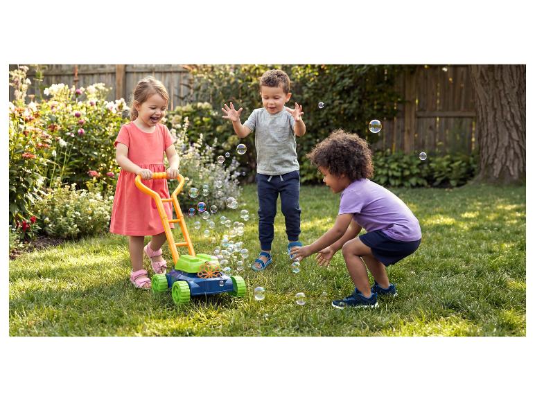 Drei glückliche Kinder spielen mit einem Blasen-Rasenmäher in einem sonnigen Garten.