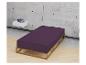 Einfaches Bett mit lila Matratzenbezug und Holzrahmen, graue Betonwand