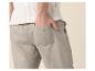 Mann in weißem Stricktop und hellgrauer Leinenhose mit Hand in der Tasche.