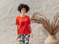 Eine Frau trägt ein orangefarbenes T-Shirt und eine Hose mit tropischem Muster.