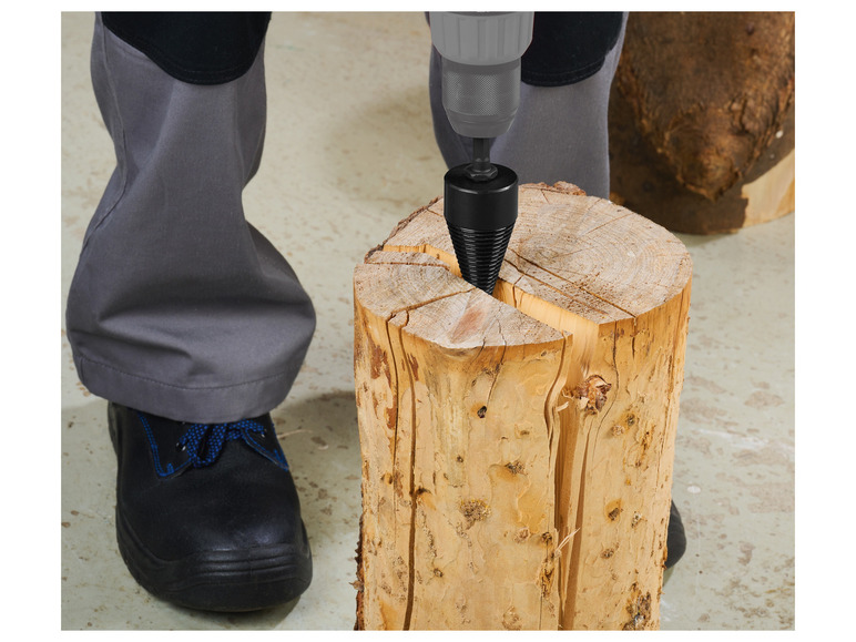 Eine Person befestigt einen Holzspalter mit einem Bohrer in einem Baumstamm.