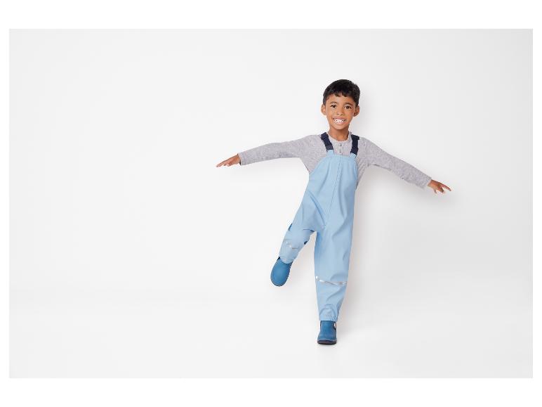 Ein Junge trägt blaue Gummistiefel und eine blaue Regenhose.