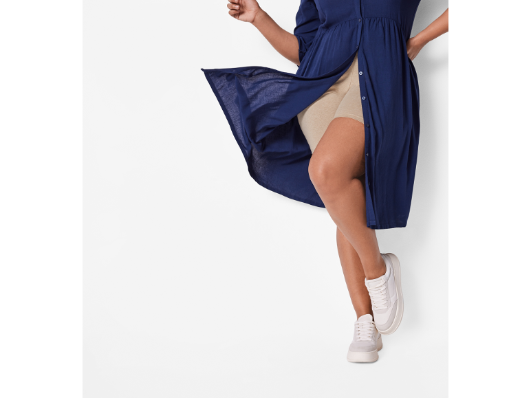 Frau in marineblauem Hemdblusenkleid und beigefarbenen Shorts, weiße Sneaker.
