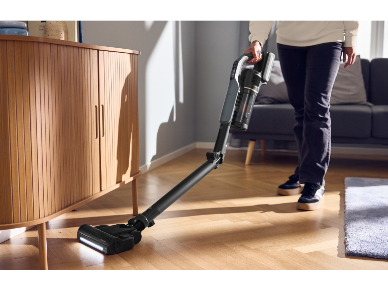 Person saugt Boden mit kabellosem Staubsauger in hellem Wohnzimmer.