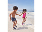 Zwei Kinder in Badebekleidung und Wasserschuhen spielen am Strand.