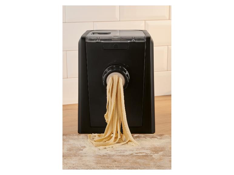 Automatische Nudelmaschine extrudiert frische Tagliatelle auf ein bemehltes Holzbrett.