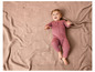 Ein Baby in einem rosafarbenen Strampler liegt auf einer gestrickten Decke.