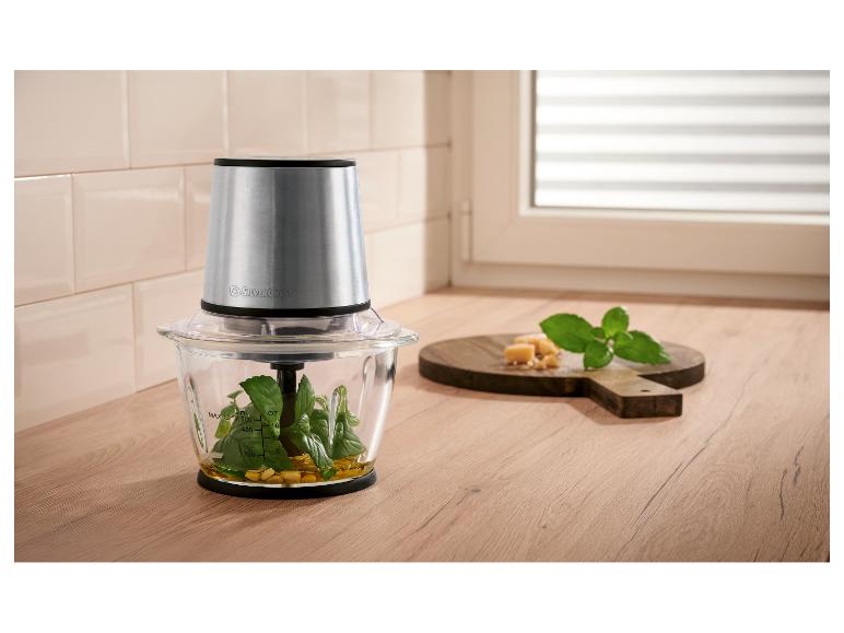 Zerkleinerer mit Basilikum, Olivenöl und Käse auf einer Holztheke.