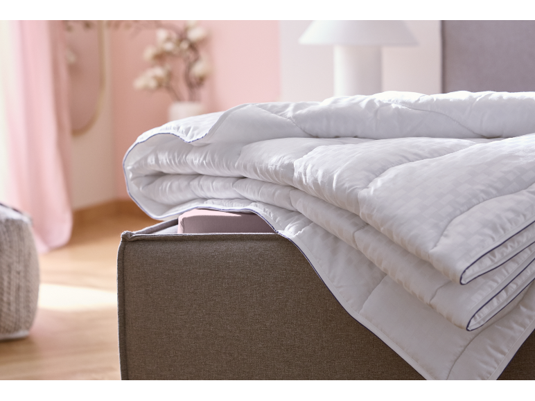 Gefaltete weiße Bettdecke mit blauem Rand auf einem Bett in einem Schlafzimmer mit rosa Wänden.