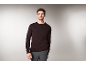 Ein Mann in einem dunkelbraunen Rundhals-Pullover und einer grauen Hose.