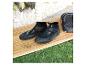 Schwarze Neoprenschuhe auf einem Holz-Surfbrett mit Gras im Hintergrund.