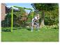 Junge in weißem T-Shirt und blauen Jeans vor einem grünen Fußballtor im Garten.