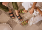 Braune und limettengrüne Sandalen auf einem karierten Teppich, getragen von Personen in Freizeithosen.